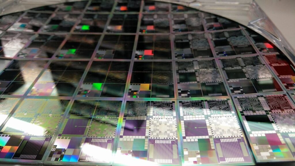 Close-up of a patterned silicon wafer with a grid of microelectronic chip dies catching iridescent light