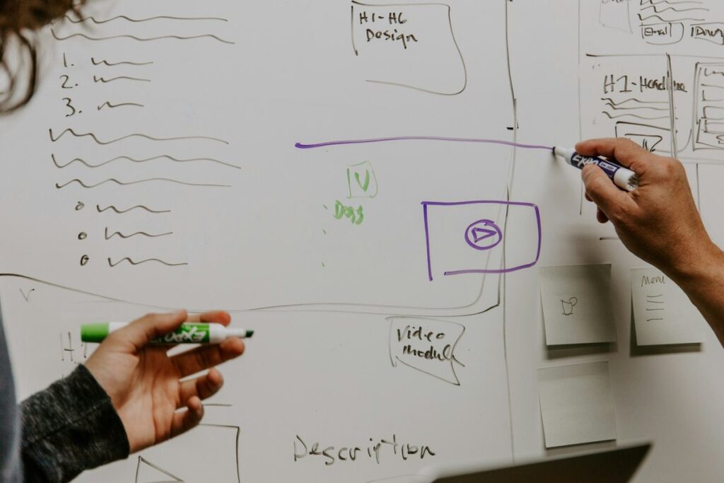 Two people's hands sketching boxes and modules of a design on a whiteboard