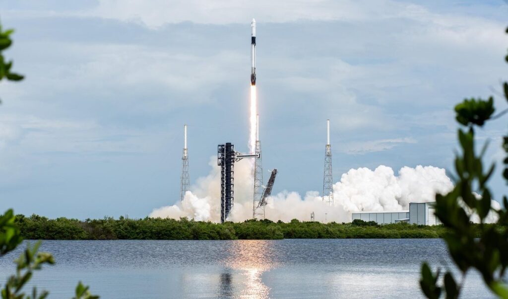 A SpaceX Falcon 9 rocket lifting off from Cape Canaveral on NASA's Crew-9 mission, its flame reflected in the water in front of the launch pad