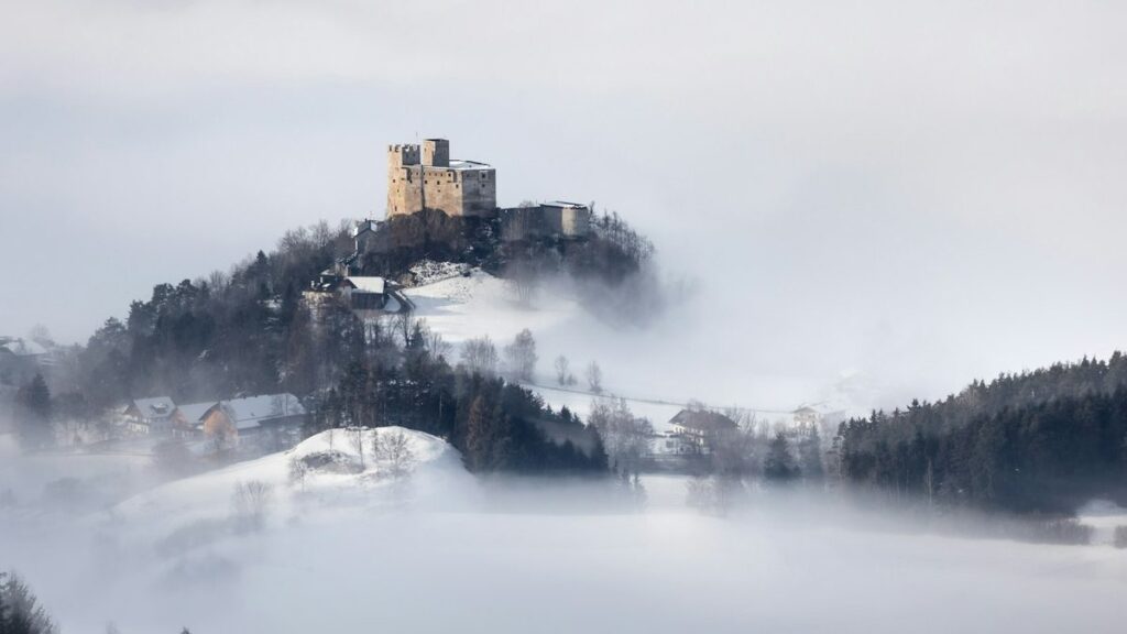 Medieval stone fortress on a snowy hilltop rising above thick morning fog in the South Tyrol mountains