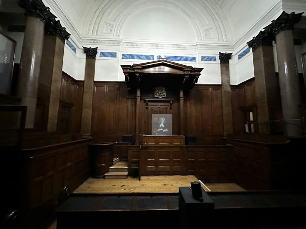 Empty wood-panelled courtroom with marble columns and the judge's bench under a carved canopy