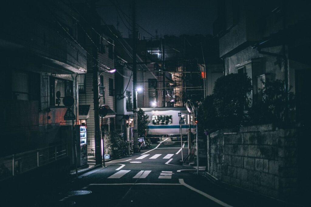 Dark, empty residential backstreet in Tokyo at night, with a lit commuter train passing at the end of the road