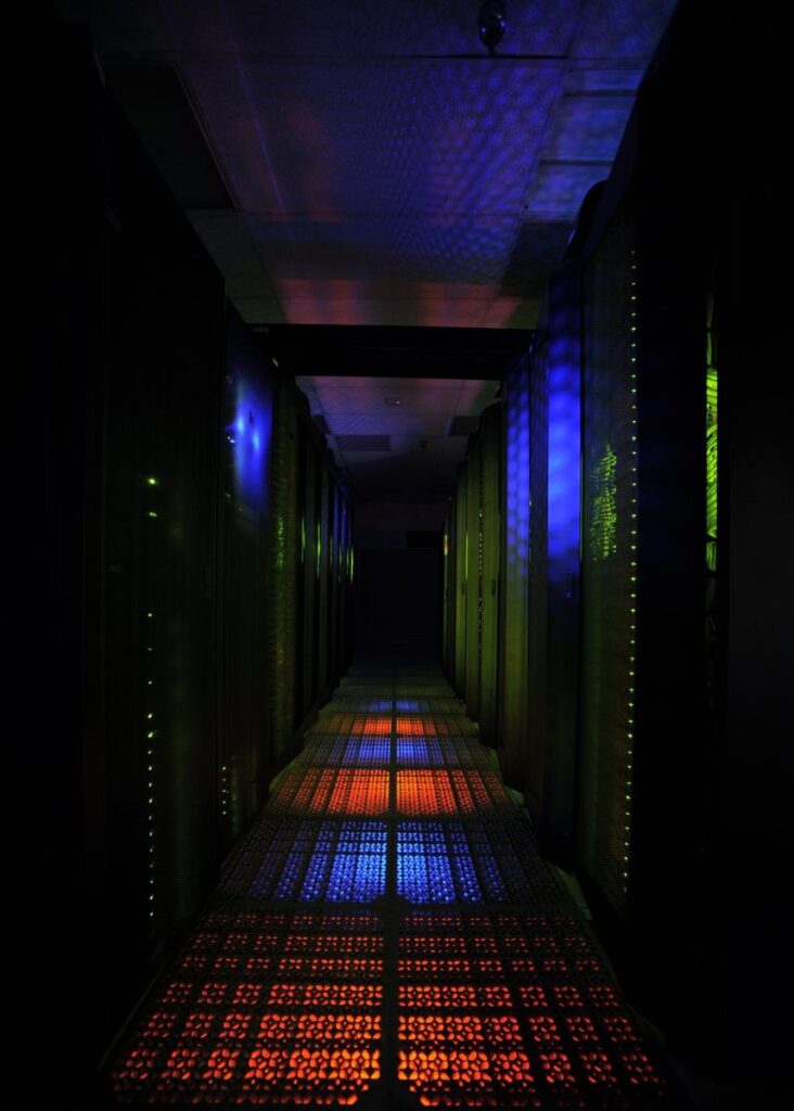 An aisle between rows of the Discover supercomputer at NASA Goddard, lit in blue, green and orange