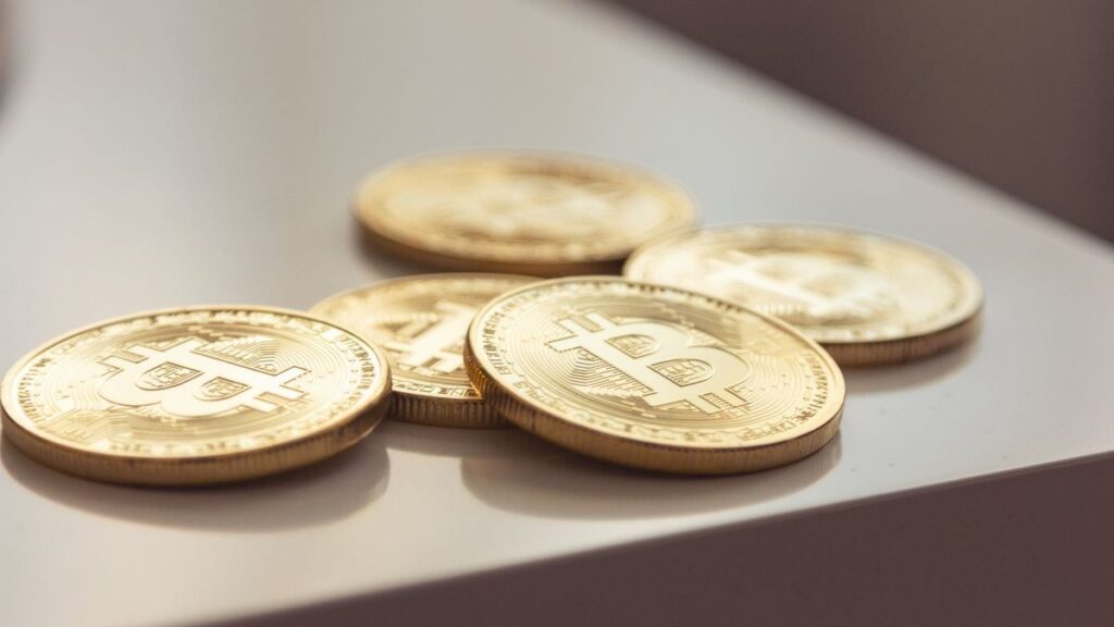 Several gold-coloured physical bitcoin coins resting on the corner of a white table