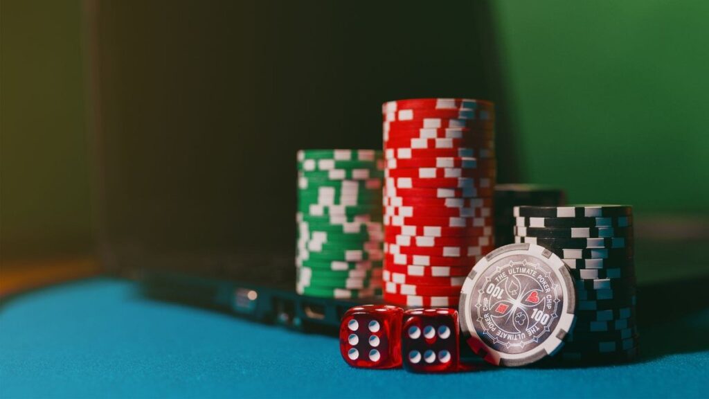 Stacks of green, red and black casino chips beside two red dice on a blue felt table