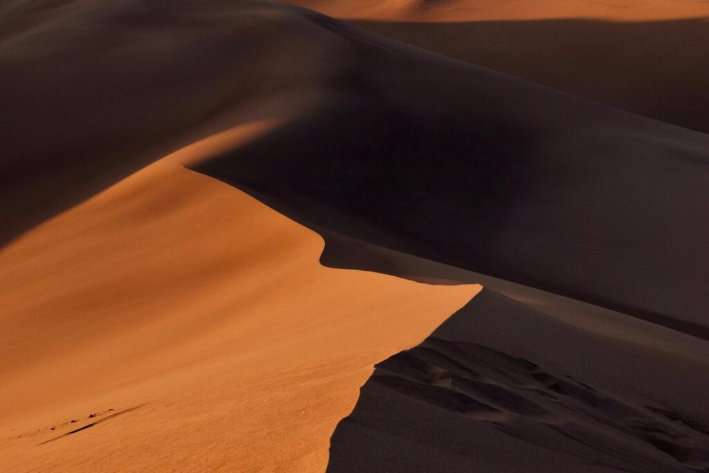 Sharp ridge of a towering sand dune lit orange by low sun, with deep shadows across the dunes behind