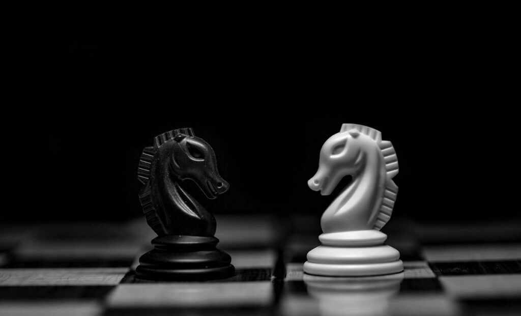 Black-and-white photo of a black and a white chess knight facing each other on a chessboard