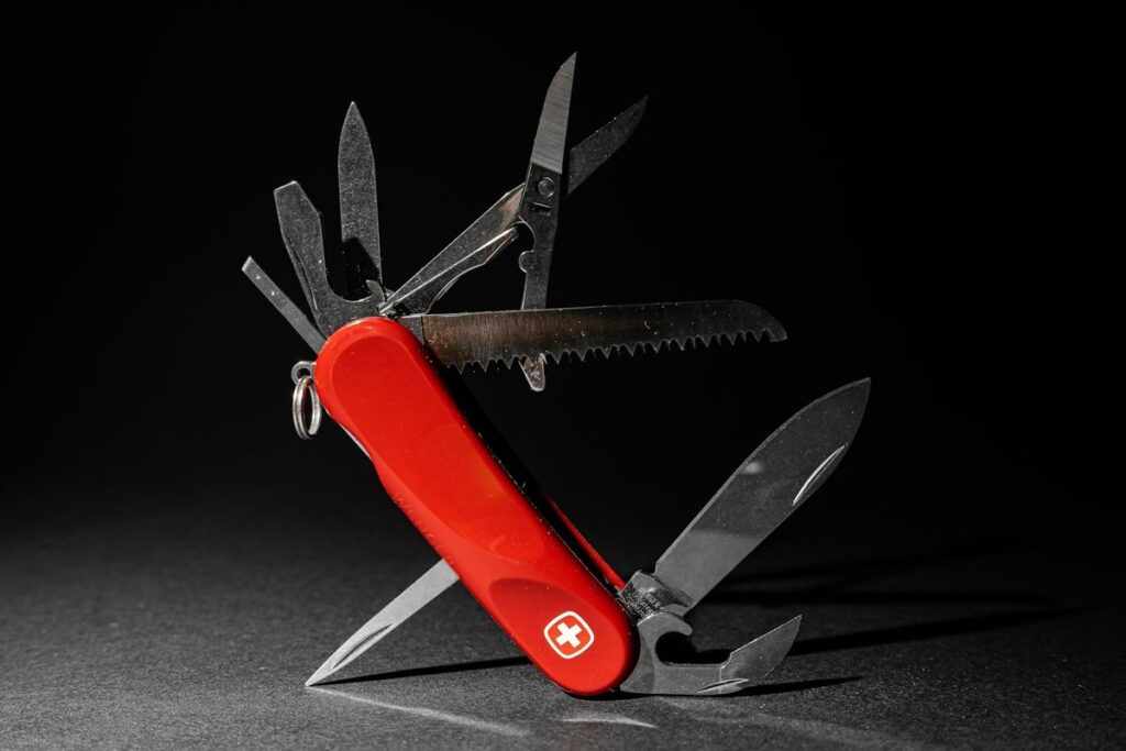 A red Swiss Army knife with all its blades, saw, scissors and tools fanned out against a black background