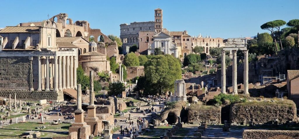 The Roman Forum in sunlight, with the Temple of Antoninus and Faustina, the three columns of the Temple of Castor and Pollux and the Colosseum behind