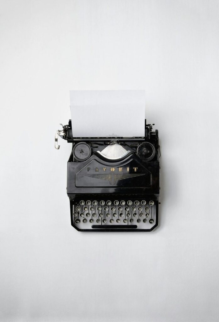 Overhead view of a black vintage typewriter with a nearly blank sheet of paper on a plain white surface